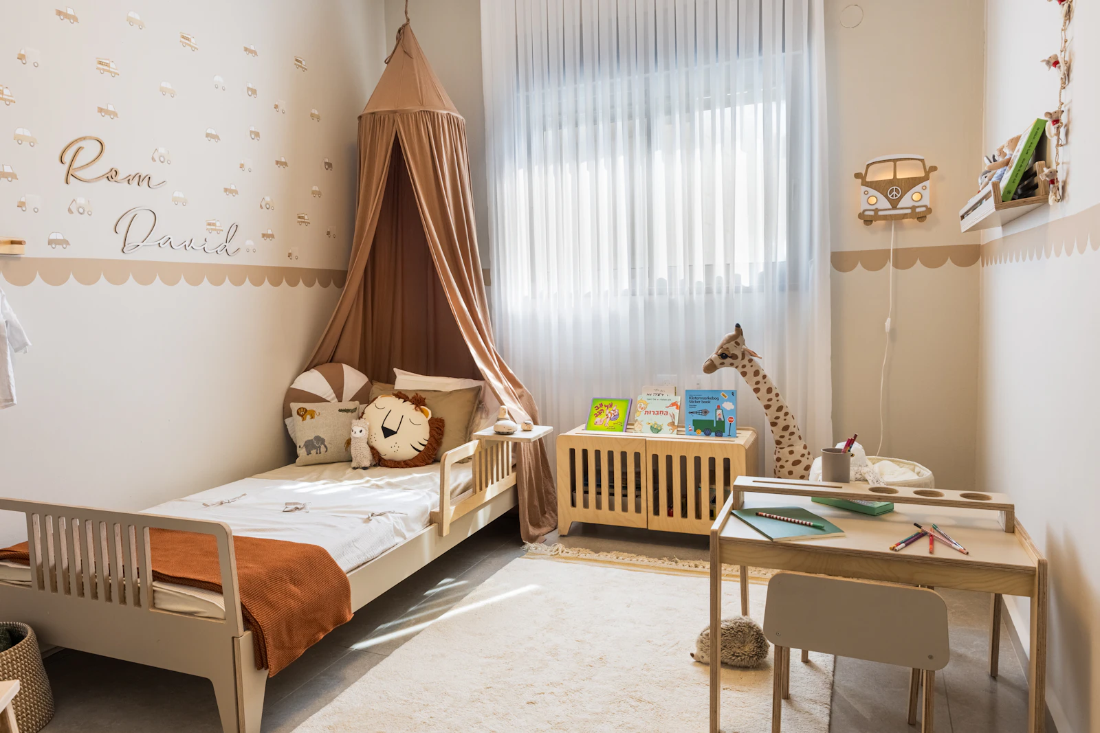 Chambre d'enfant aux tons beige clair avec voilage léger, ciel de lit et petit bureau