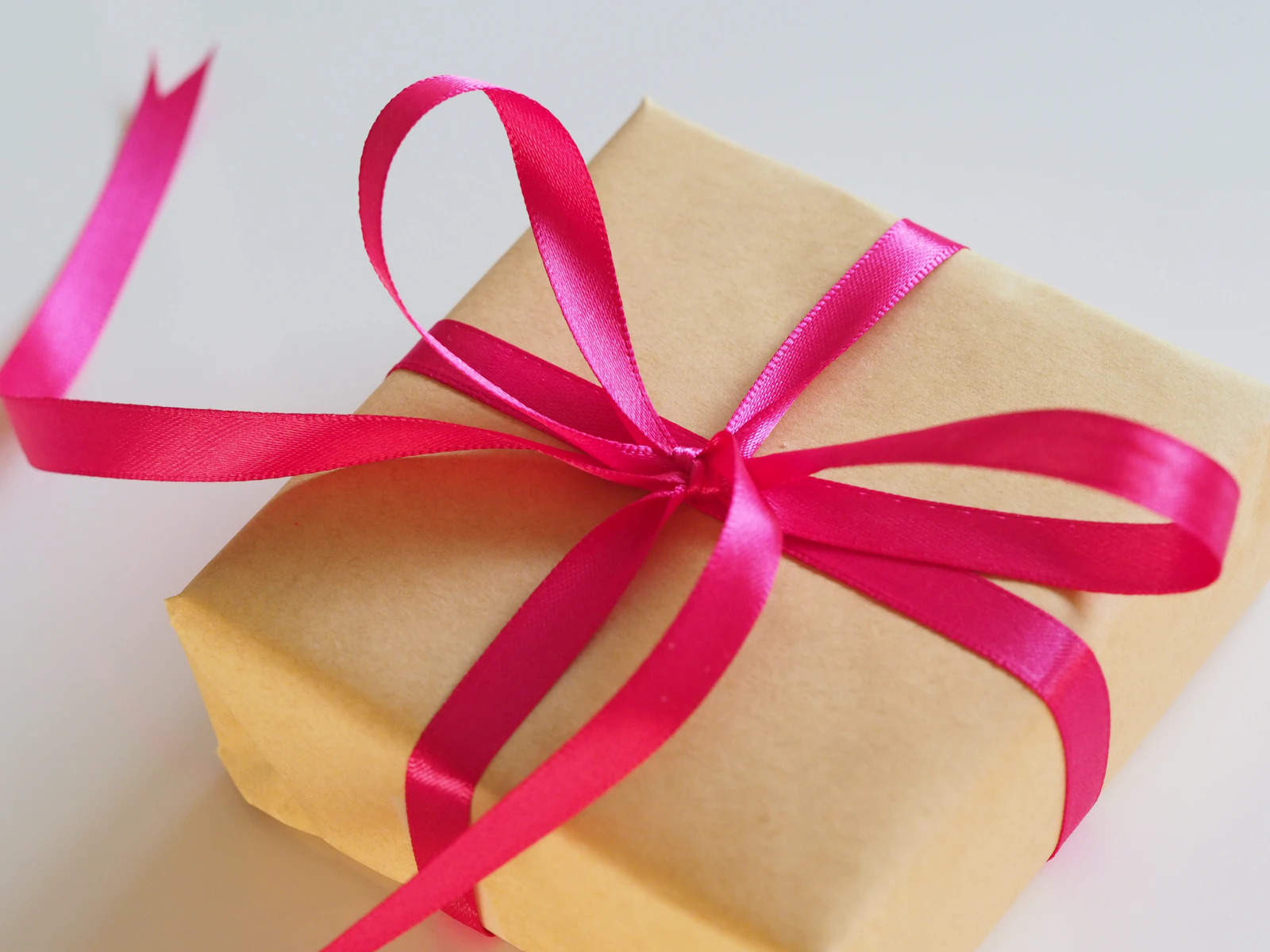 Paquet cadeau en papier kraft fermé par un large ruban rose vif