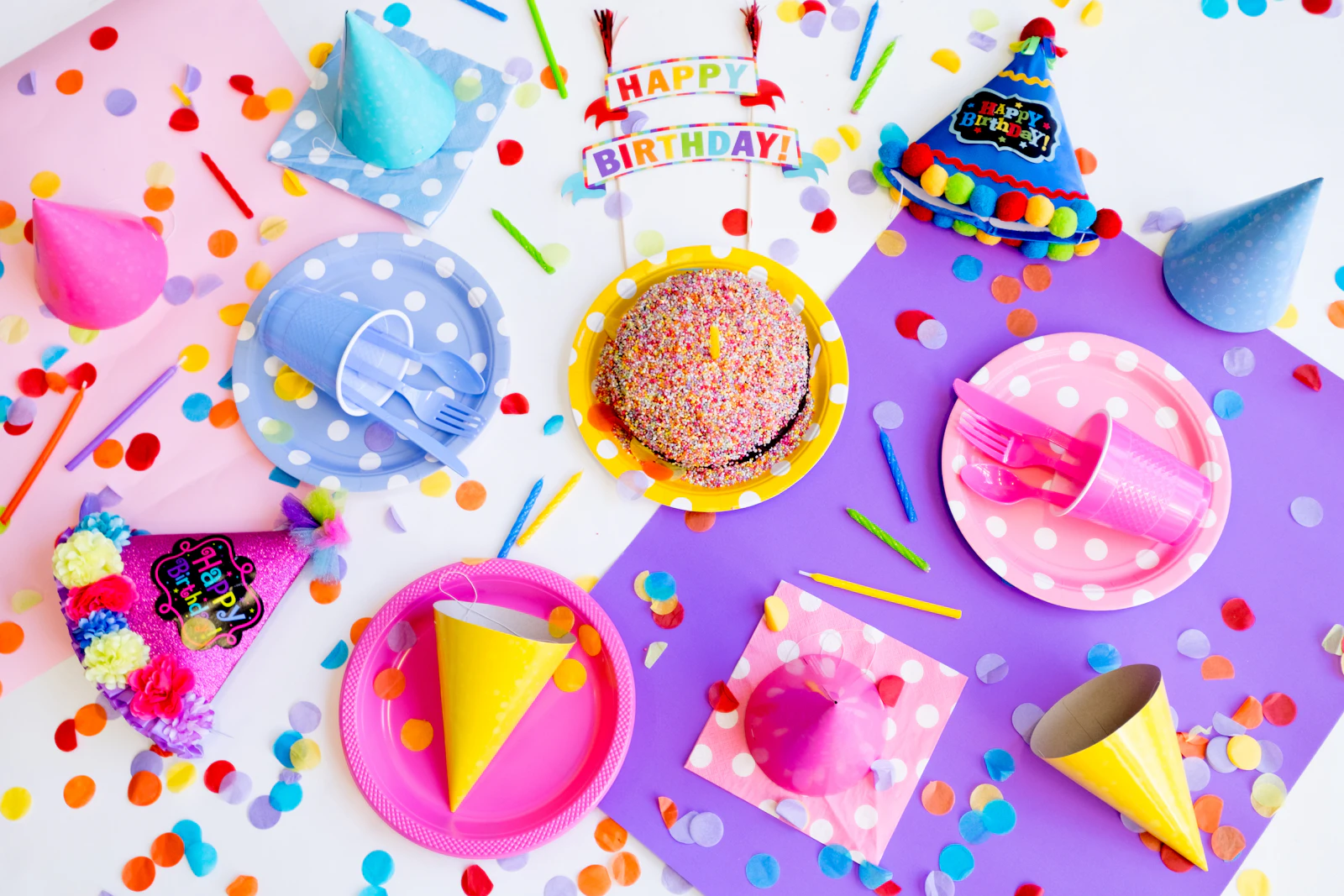 Table d'anniversaire vue du dessus avec chapeaux pointus, assiettes colorées et confettis