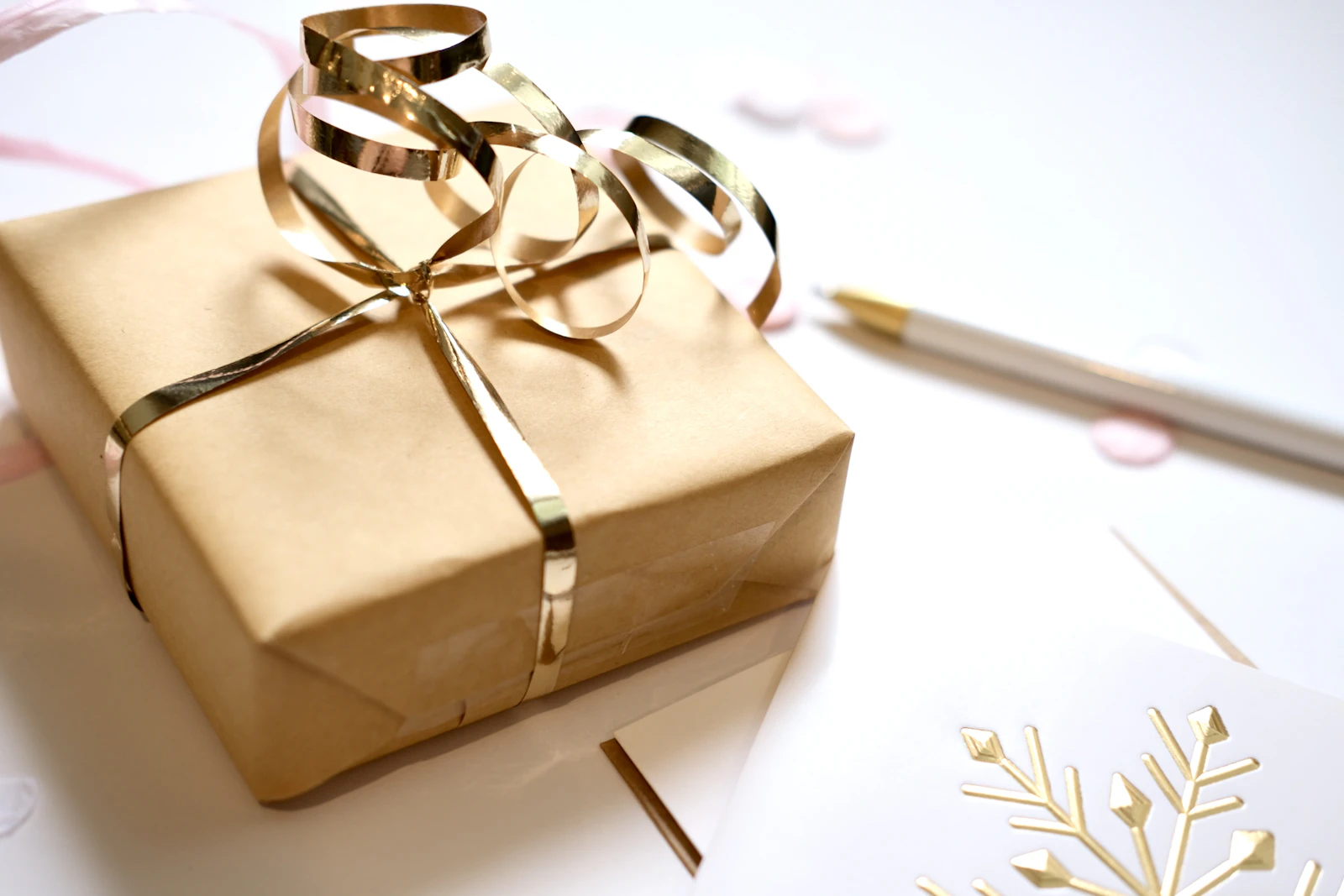 Paquet cadeau en papier kraft noué d'un ruban doré, près d'un stylo blanc