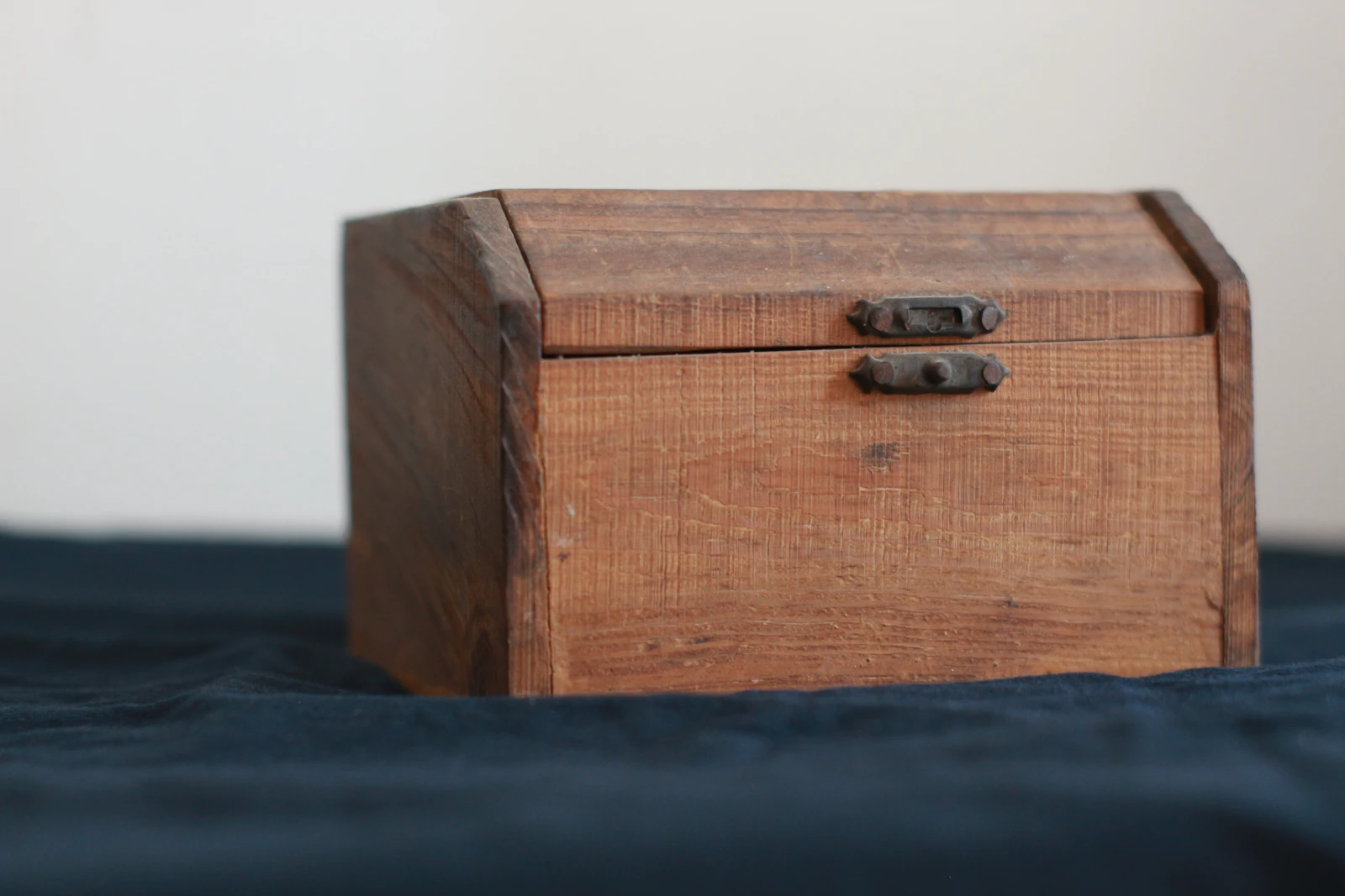 Boîte en bois ancienne à fermoirs métalliques posée sur un tissu bleu sombre