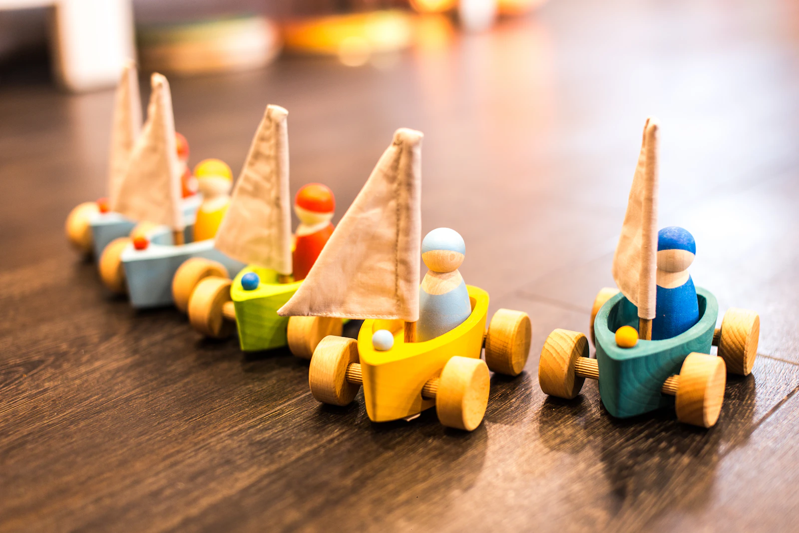 Petites voitures en bois colorées avec voile et personnages, alignées sur un parquet