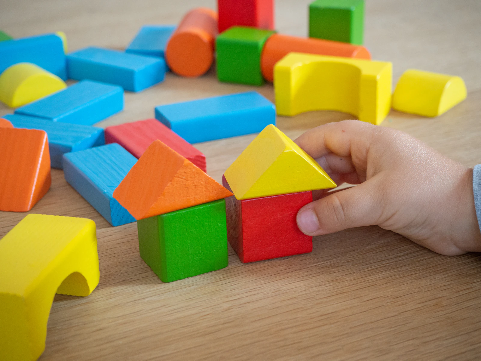 Main d'enfant posant un toit triangulaire sur des blocs de bois colorés