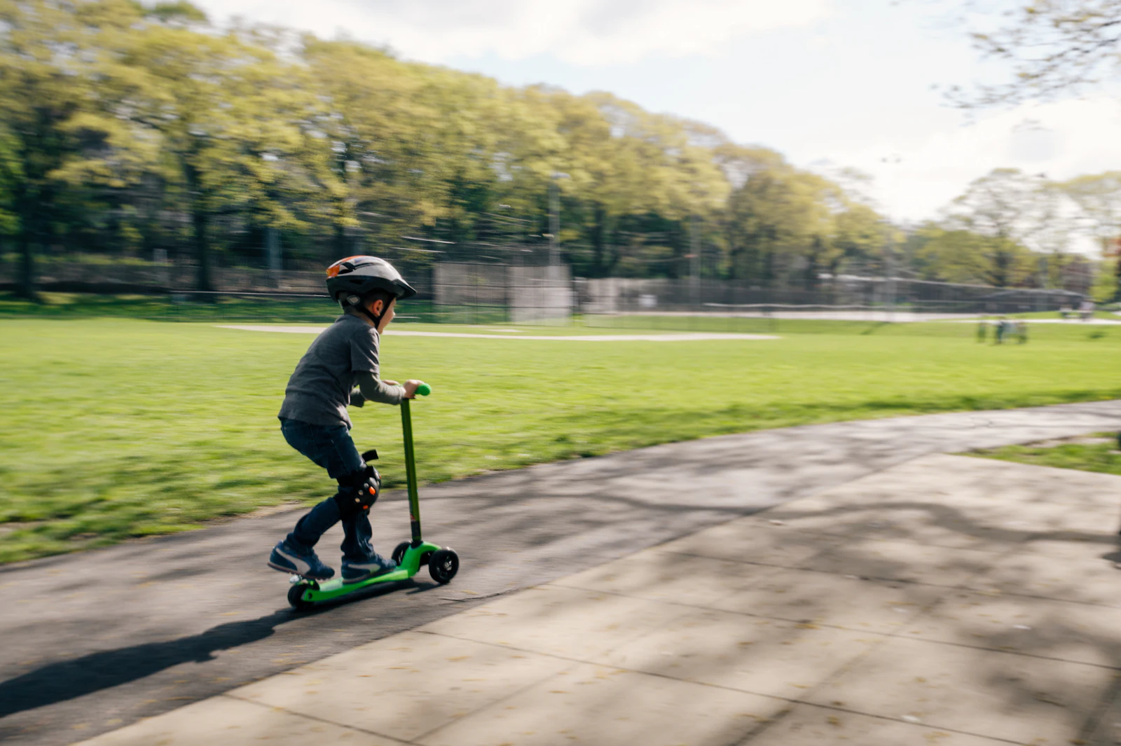 Petit garçon casqué roulant en trottinette verte sur une allée de parc