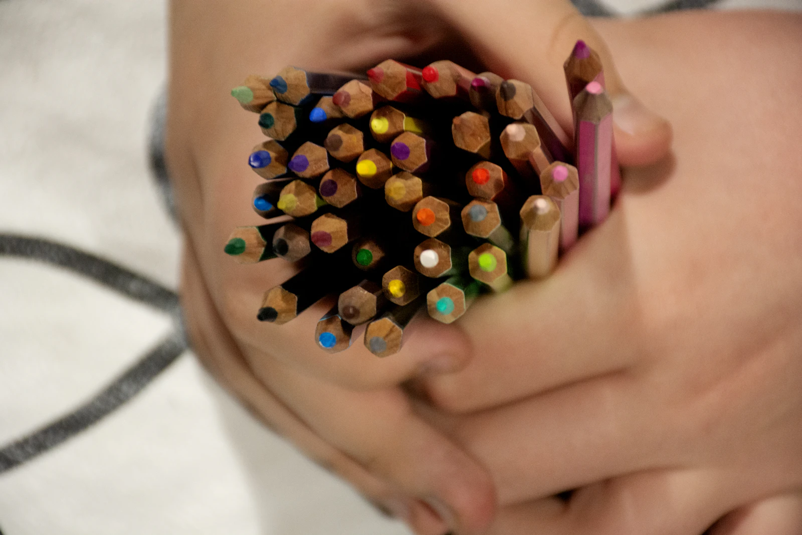 Deux mains serrant un gros bouquet de crayons de couleur en bois