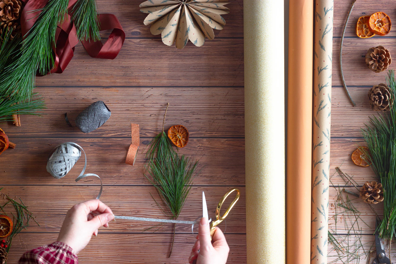 Mains d'adulte préparant un emballage de Noël avec ficelle, ciseaux et branches de sapin