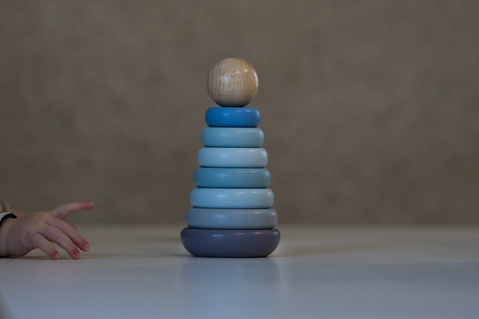 Main de bébé tendue vers une pyramide d'anneaux en bois aux tons bleus