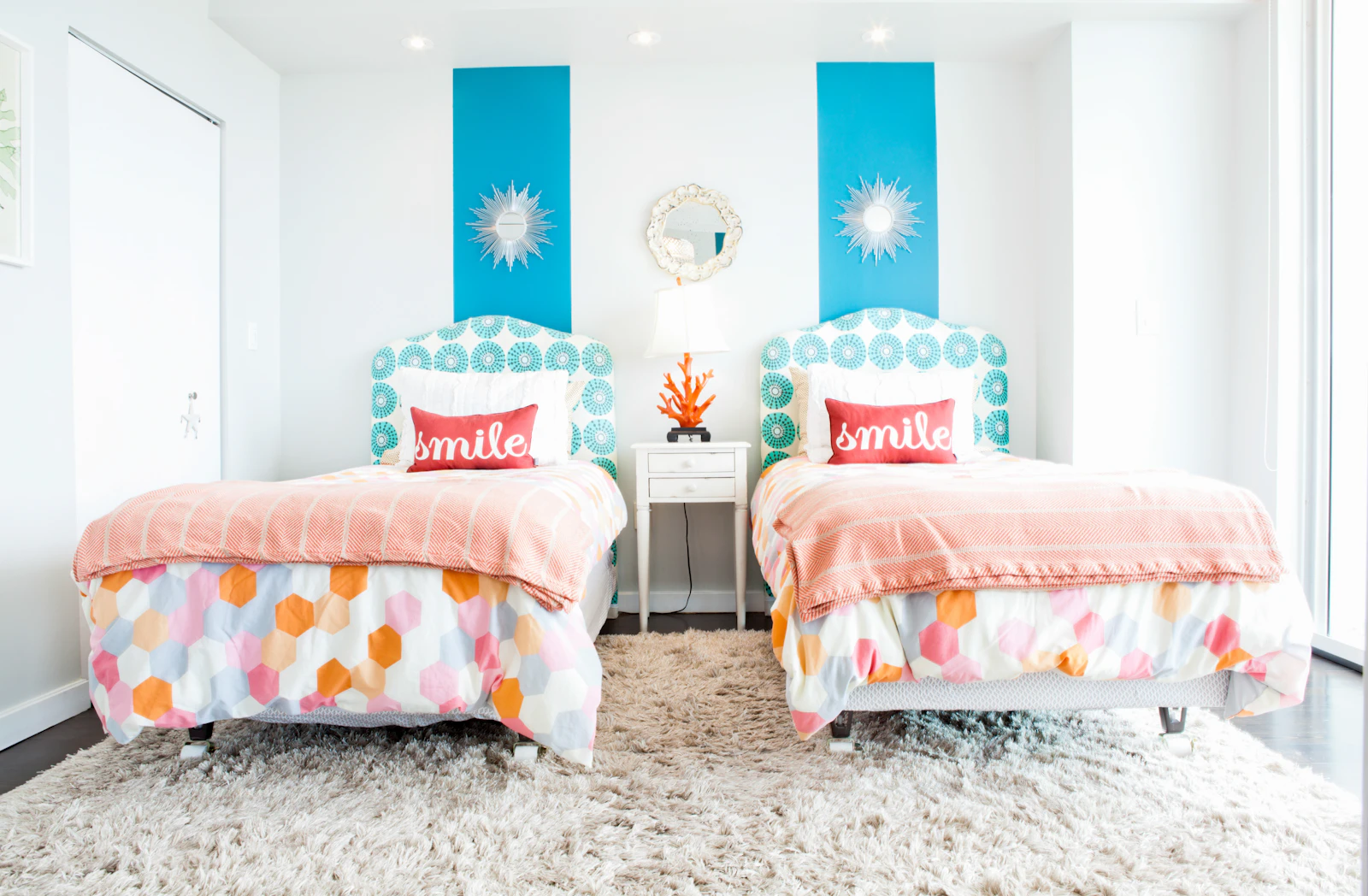 Deux lits jumeaux aux couettes colorées côte à côte dans une chambre lumineuse