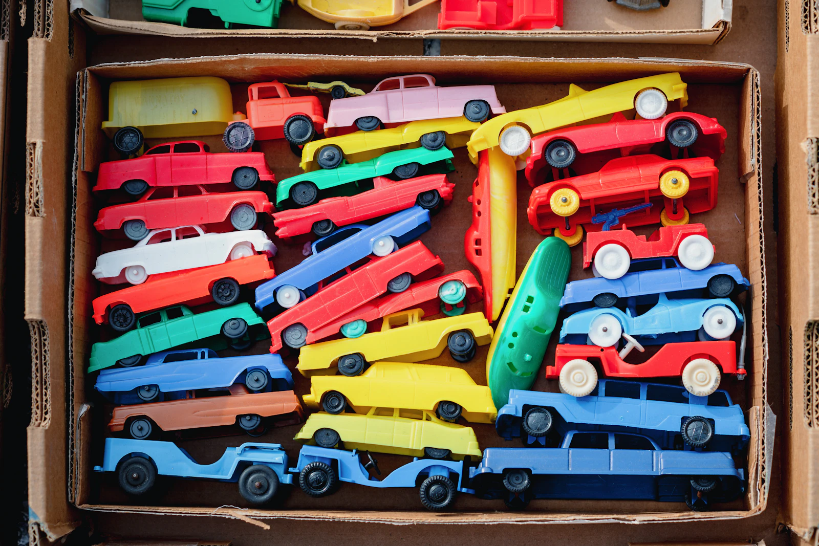 Carton rempli de petites voitures anciennes en plastique de toutes les couleurs