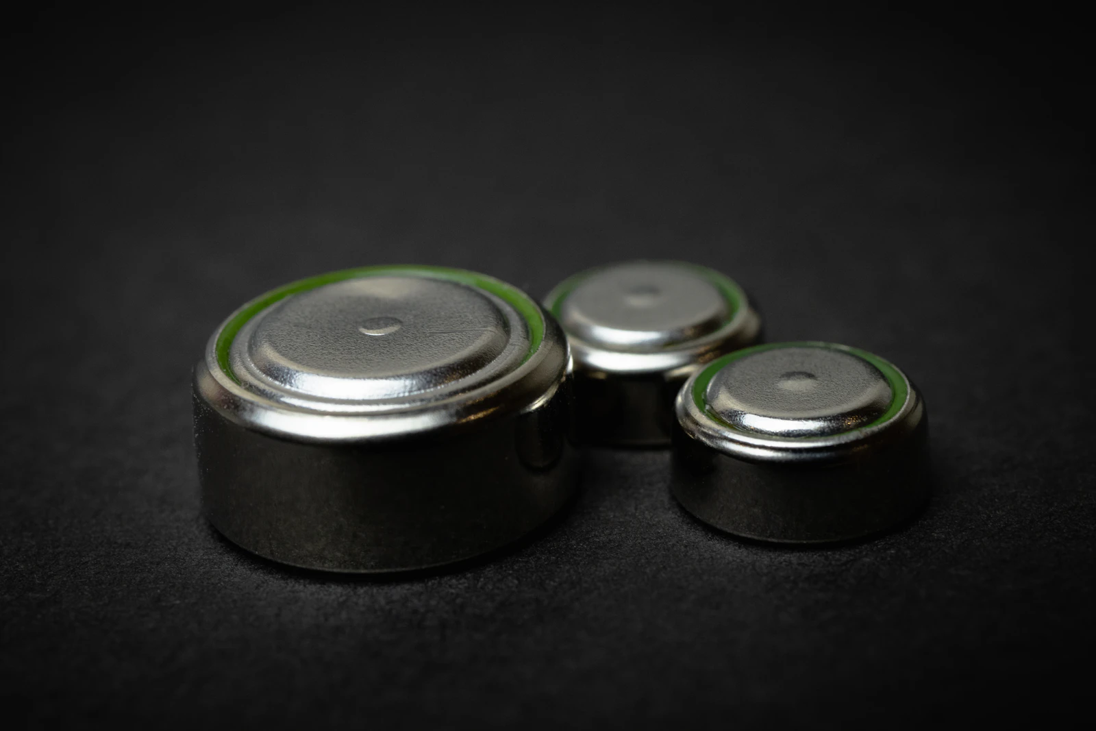 Trois piles bouton argentées de tailles différentes posées sur un fond noir