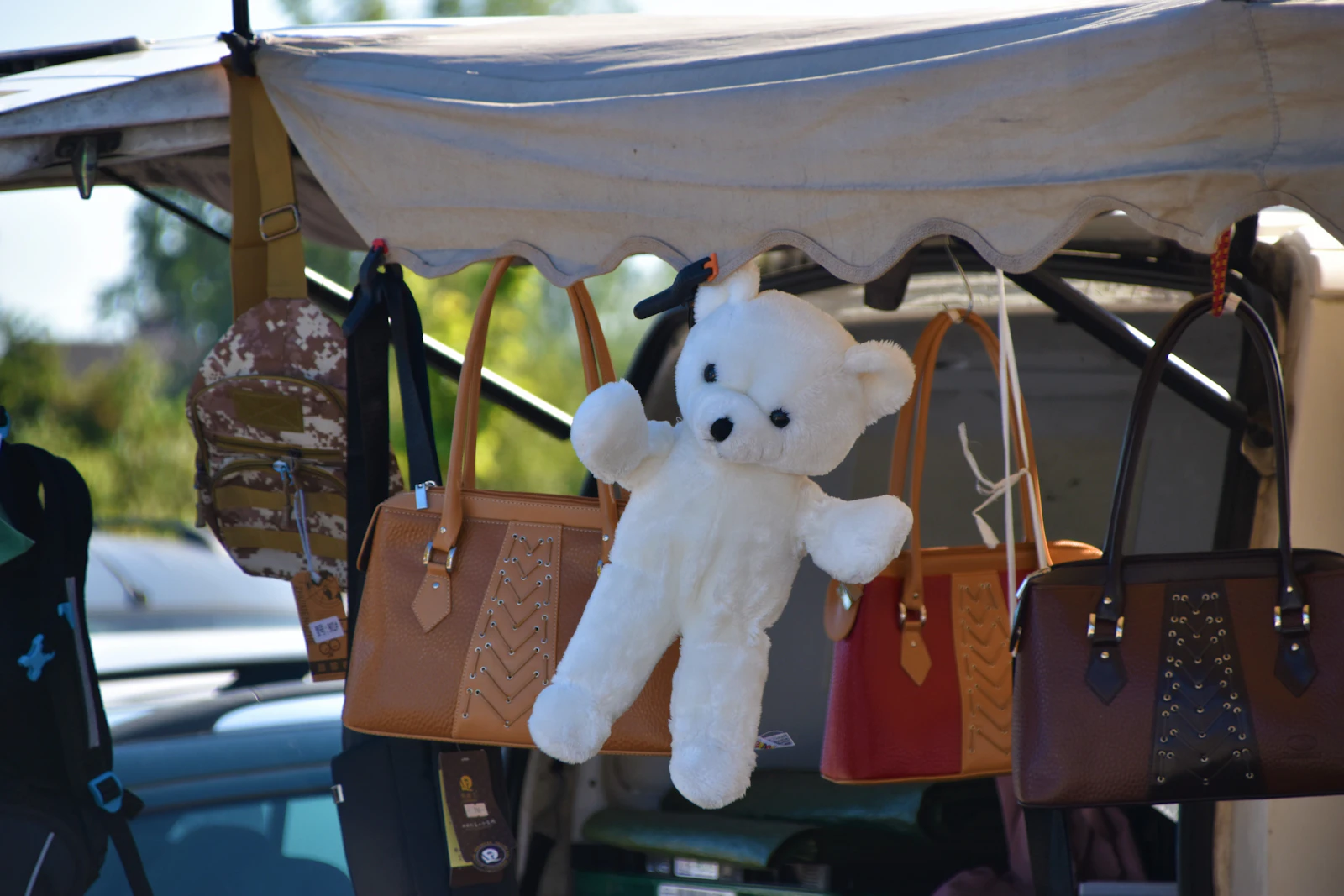 Ours en peluche blanc suspendu à un stand de brocante entre des sacs à main