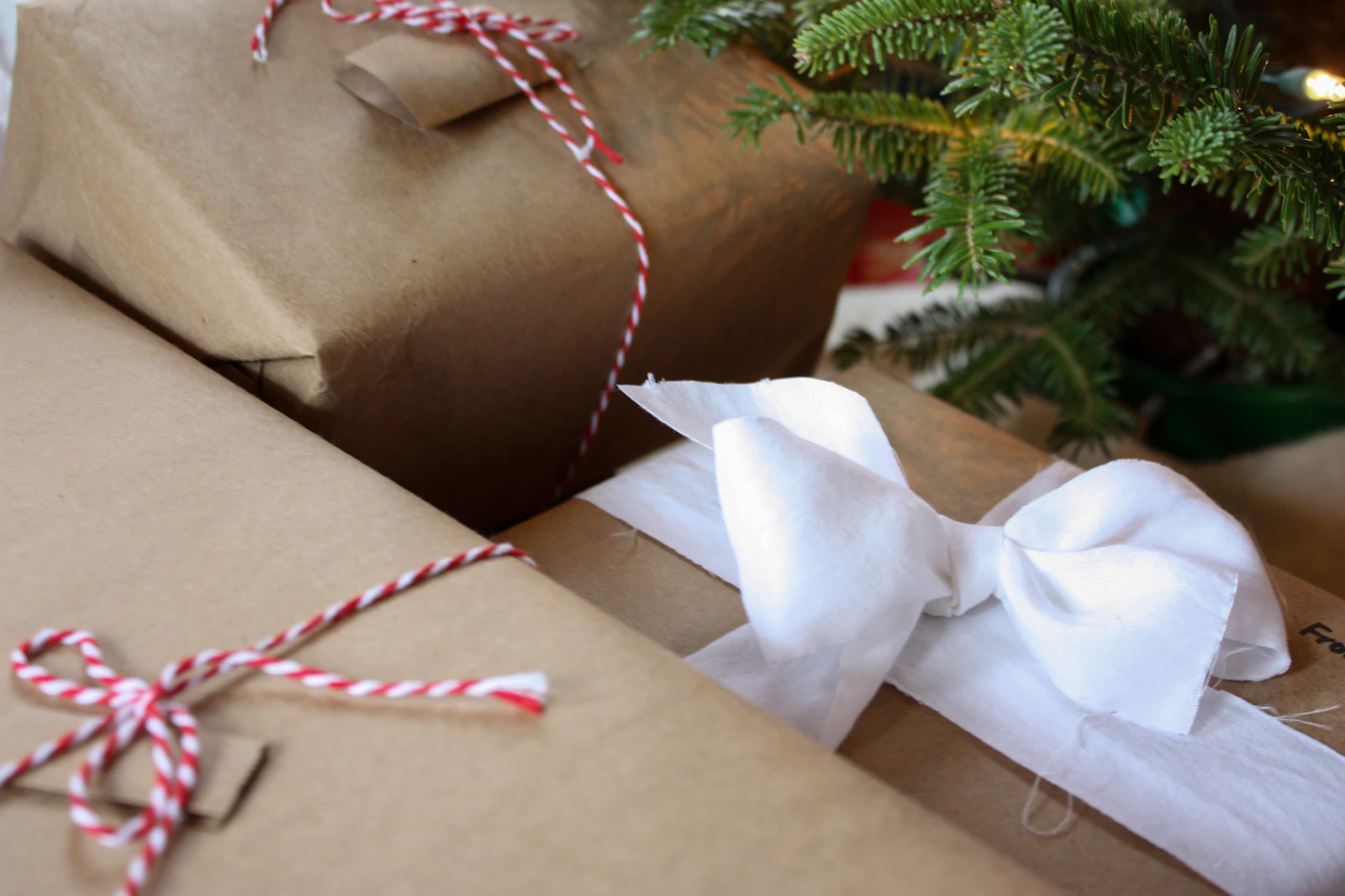 Cadeaux emballés dans du papier kraft avec ficelle rouge et blanche au pied du sapin