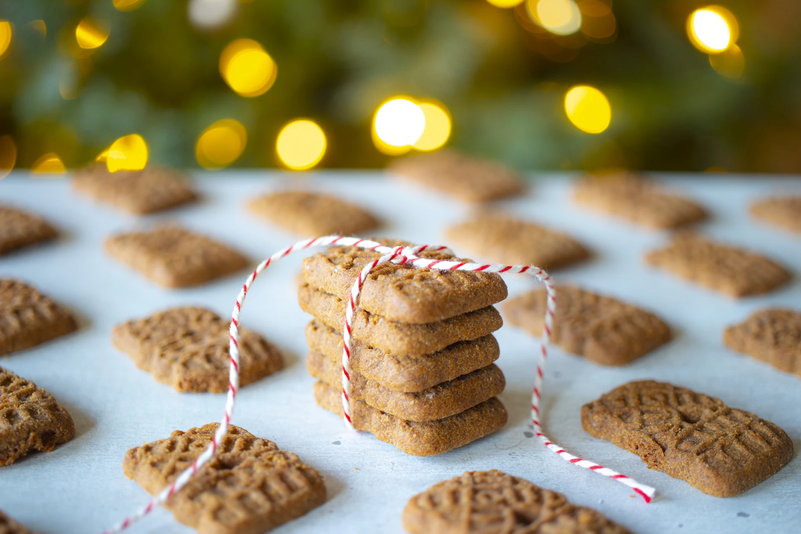 Pile de spéculoos ficelée de rouge et blanc devant les lumières d'un sapin
