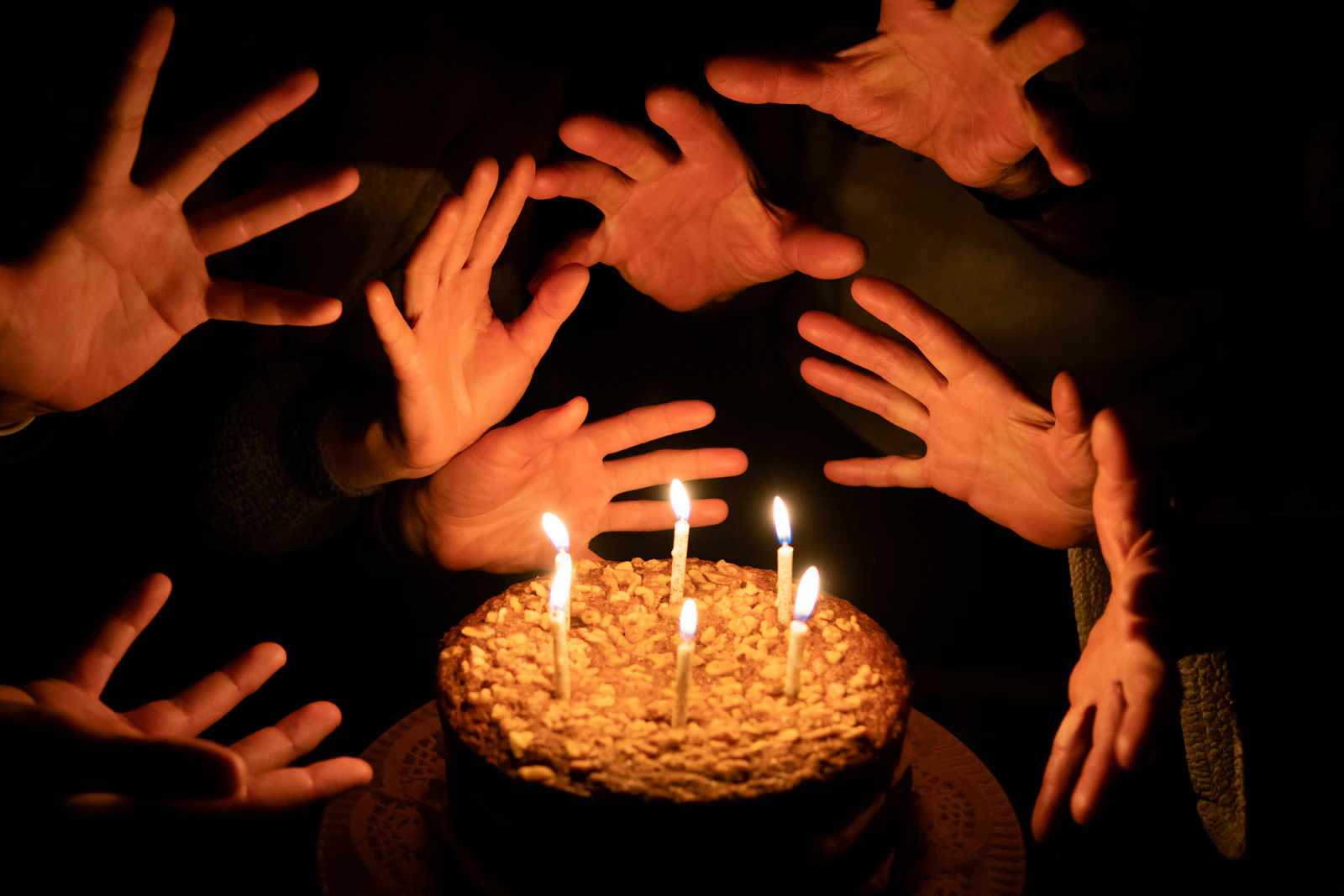 Mains de plusieurs membres d'une famille tendues vers un gâteau d'anniversaire aux bougies allumées